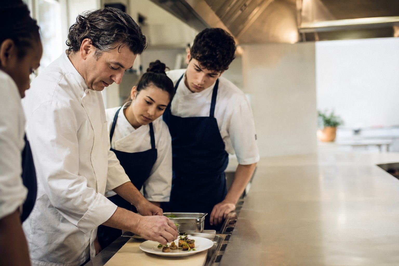 Un chef instructeur transmet un geste de dressage à de jeunes apprentis en cuisine professionnelle